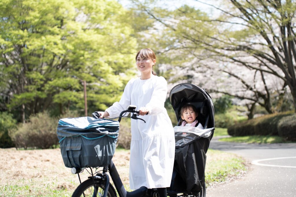 子どもを後部座席に乗せた電動自転車を押す女性