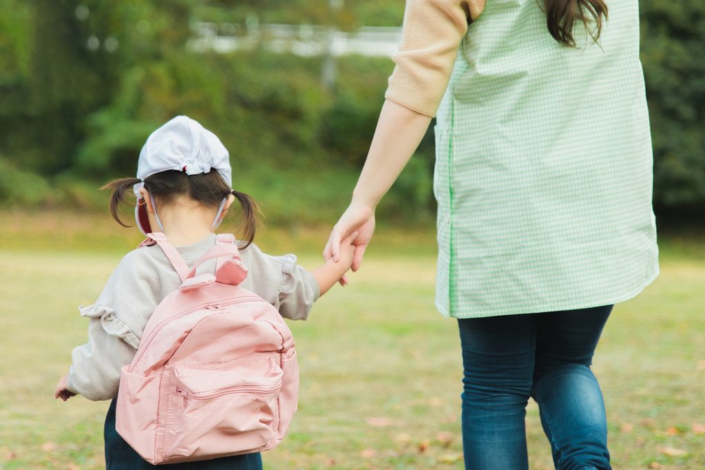 保育士と手をつないで登園する幼児の後ろ姿