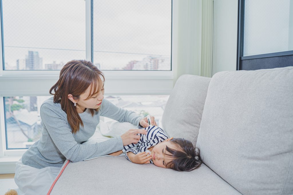 発熱した子どもをソファで看病する母親